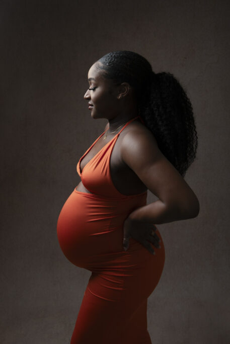 Future maman en robe orange lors d’une séance grossesse en studio